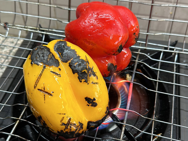 金属的全画幅图像，厨房炉子的煤气灶的橙色和蓝色火焰上的烹饪篮，红色和黄色的灯笼椒，炭烤水果和蔬菜，重点在前景图片下载