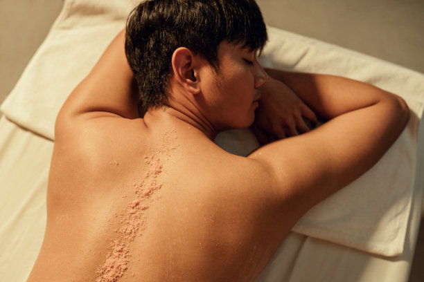 亚洲男士的背部有选择性的盐磨砂，放松男士的背部有按摩师的皮肤护理磨砂按摩。搓澡和护肤概念。图片下载