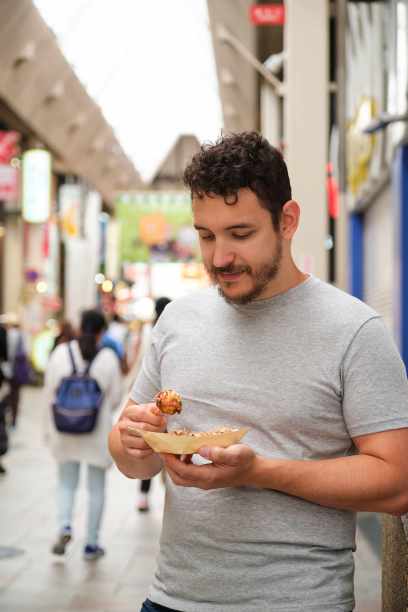 在日本大阪的道顿堀街，一名拉丁青年正在吃章鱼烧。图片下载