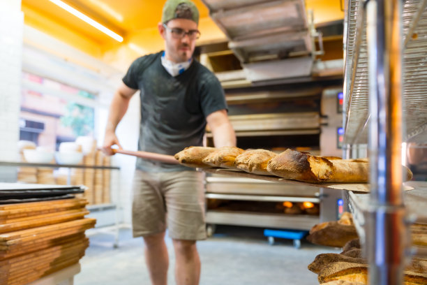 工匠作坊里的面包师把烤箱里的面包放在架子上图片下载
