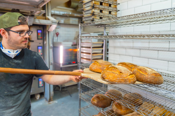 面包师在面包店车间把从烤箱里取出的面包放在货架上，在商店里出售图片下载