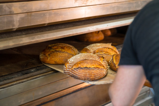 车间面包店男员工面包师手工面包店车间从烤箱中取出烤好的面包图片下载