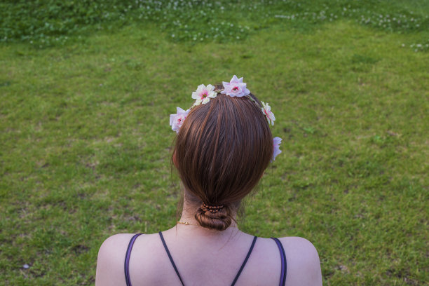 头发装饰的年轻女孩看着绿草草坪的特写镜头。瑞典。图片下载