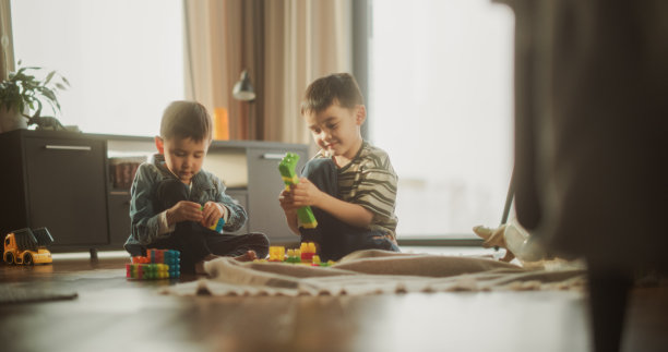 两个亚洲男孩在阳光明媚的日子里在房间里玩彩色积木的照片。哥哥帮弟弟搭玩具屋。童年和纯真的概念图片下载
