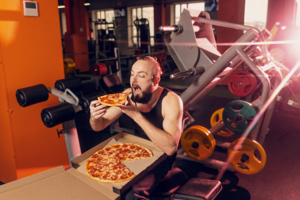 一个留胡子的年轻人很高兴在健身房吃披萨。图片下载