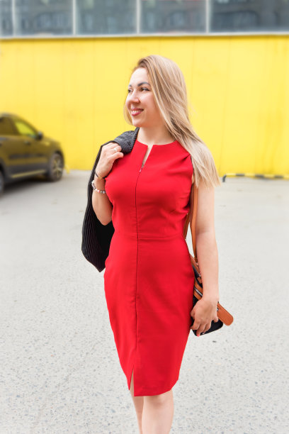 一个穿红裙子的年轻女子站在停车场，城市生活。商业女性,黄色的墙图片下载