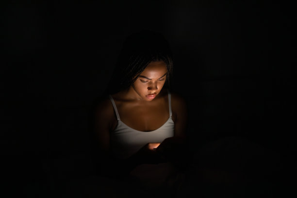 非裔美国妇女晚上躺在床上看手机。图片下载