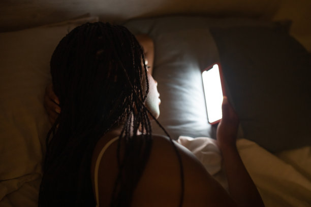 非裔美国妇女晚上躺在床上看手机。图片下载
