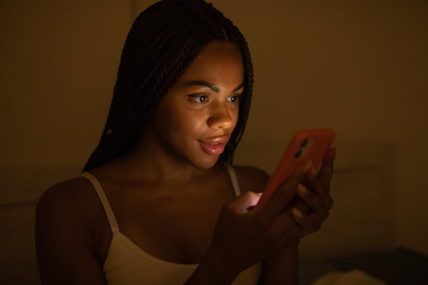 非裔美国妇女晚上躺在床上看手机。图片下载