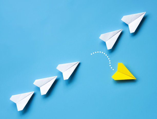 黄色纸飞机折纸在蓝色背景上留下其他白色飞机，可为文本或想法定制空间。领导概念和复制空间。图片下载