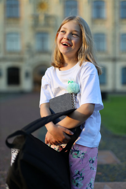 快乐的一年级女孩背着书包在校园里。图片下载