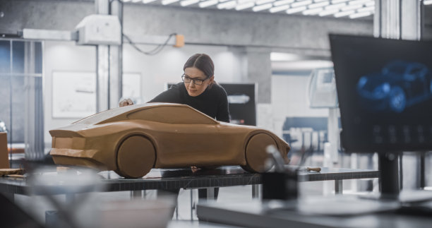 汽车设计师在计算机上使用3D软件。近距离在屏幕上的焦点和女性建模师创建一个粘土模型的汽车。在产品设计机构工作的年轻专家团队图片下载