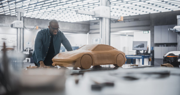 非洲汽车设计师用抹刀用聚合物模型粘土制作汽车原型。在一家汽车生产厂的研究和开发工作室工作的重点黑人建模师图片下载