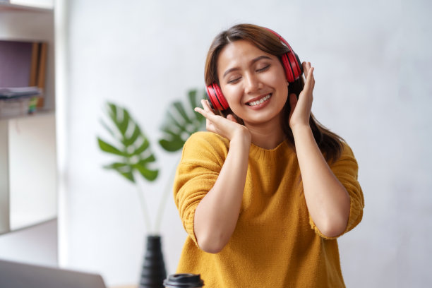 可爱的亚洲女人戴着耳机坐在家里开心地听音乐。图片下载