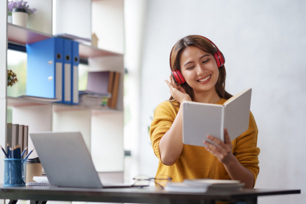 漂亮的亚洲女商人坐在笔记本电脑上，戴着耳机听音乐，看书，放松地思考工作的新想法。图片下载