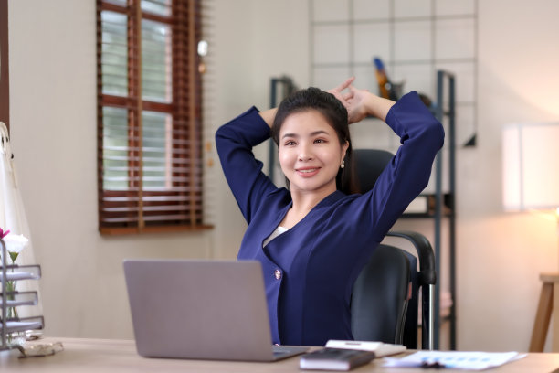 年轻的亚洲女商人伸展双臂，闭上眼睛，放松在办公室工作了一整天的疲劳肌肉。图片下载