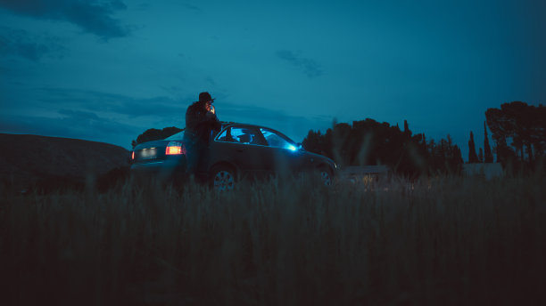 黄昏时分，一名男子在灯火通明的汽车旁吸烟的电影场景图片下载