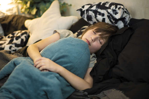 男孩抱着鲨鱼睡着了。孩子躺在枕头上，床上铺着黑白的亚麻布图片下载