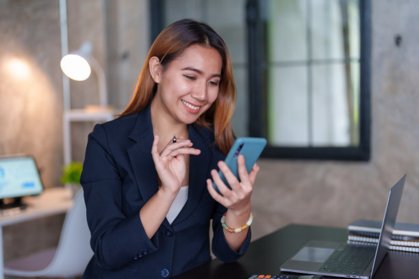 美丽的亚洲女商人在办公室用智能手机联系客户，回复聊天，在社交媒体应用程序上交易，脸上带着微笑。图片下载
