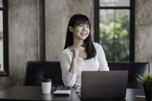 美丽的亚洲女商人正在考虑新的想法，她的工作与明亮和快乐的脸。图片下载