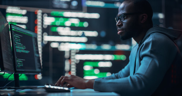 专注的黑人男性程序员在监控室工作，周围是显示编程语言代码的大屏幕。一个人的肖像创造一个软件和编码图片下载