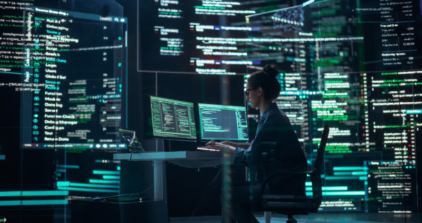 在监控室工作的职业女性程序员，周围是显示编程语言代码行的大屏幕。创建软件和编码的女性肖像图片下载