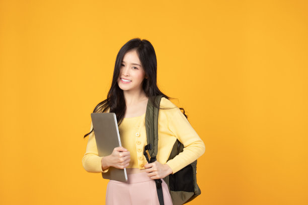 肖像快乐休闲的亚洲女学生与背包和笔记本电脑孤立的黄色背景。回归学校和学习理念。图片下载