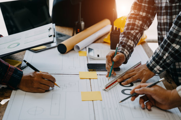 作为一个团队工作的商人在办公室的办公桌上讨论数据工作和平板电脑，笔记本电脑和建筑项目。图片下载