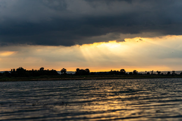 一束光穿过背景中的乌云。水面和山脉之上，泰国图片下载