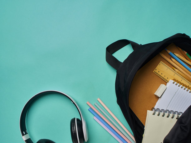 背包与不同的彩色文具在蓝色背景，顶视图。图片下载