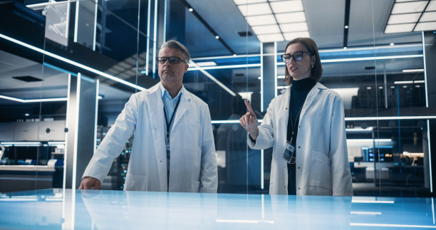 站在高科技实验室桌子旁边的白人男女科学家。专业的工业工程师在桌子上打手势。增强现实编辑的模型模板。图片下载