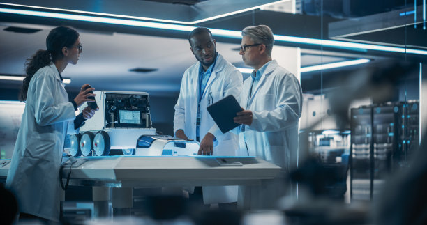 不同的工业机器人专家团队聚集在一个移动机器人的桌子旁。穿着实验室大褂的工程师讨论人工智能的自动机器人送货助手图片下载