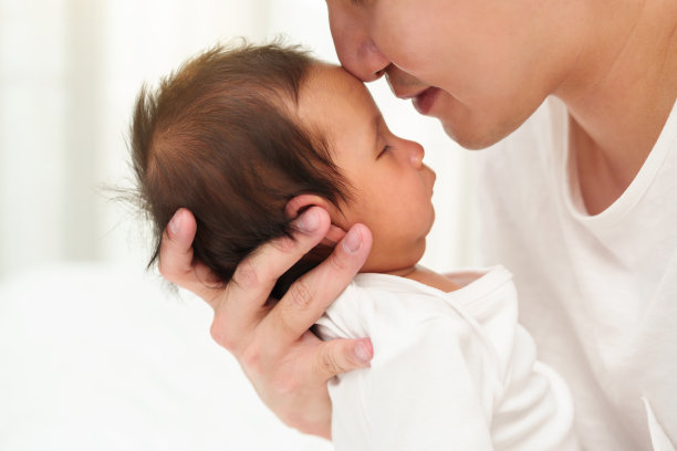 父亲在床上亲吻新生婴儿的额头图片下载