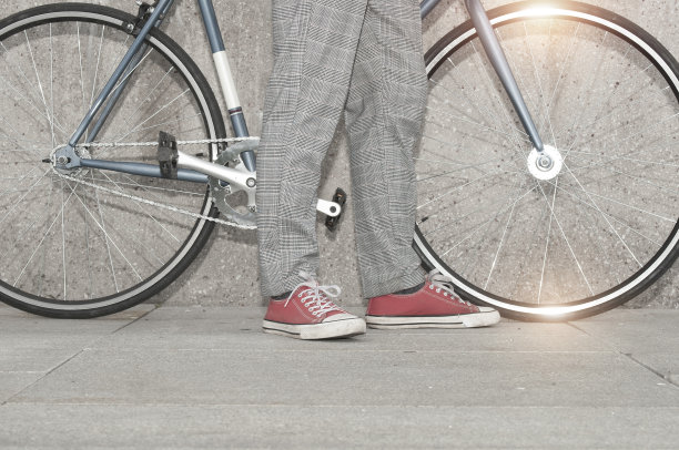在城市的水泥墙旁，一个穿着复古的男人骑着他的固定齿轮自行车图片下载