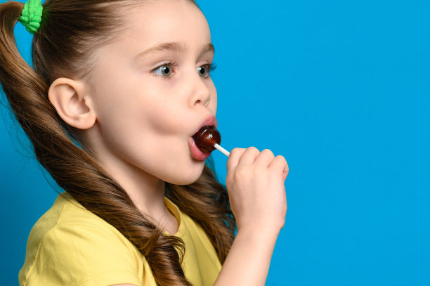 在蓝色背景上，一个女孩舔着一个圆形的棒棒糖图片下载