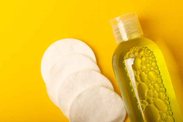 卸妆用胶束水和化妆棉。清洁皮肤的皮脂和化妆品。黄色背景的构图。美丽的概念。复制空格文本。平躺图片下载