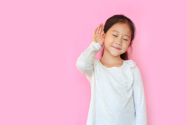 闭上眼睛，亚洲小女孩微笑着用手捂住耳朵，听着粉红色孤立的背景和复制空间的谣言或八卦。图片下载