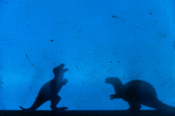 蓝色墙壁上黑色恐龙的剪影。食肉动物和食草动物。创意背景与小型微缩。有选择性的重点。副本的空间。图片下载