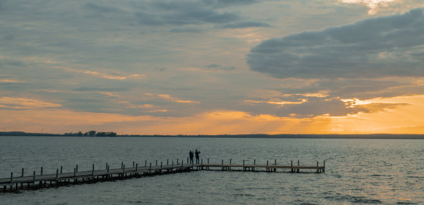 夕阳与阳光和剪影夫妇站在码头与移动摄影在湖图片下载