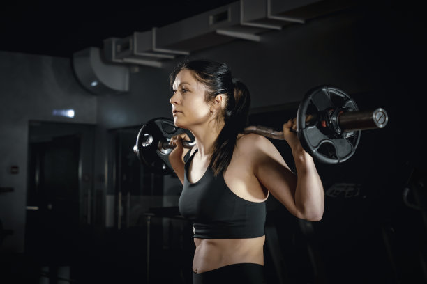 侧视图运动妇女在性感的运动服举重杠铃在健身房的背景。迷人的年轻运动肌肉女人在健身房锻炼。综合健身训练。举起杠铃图片下载