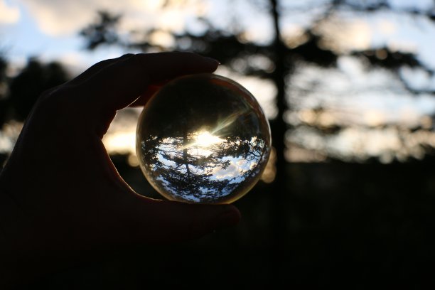 一个人的手拿着一个玻璃球，透过它看到日落的特写图片下载