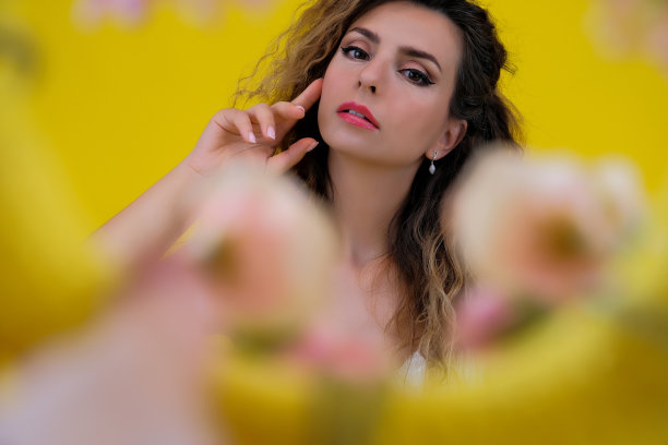 一个美丽女孩的特写肖像在黄色的背景。女子在五彩缤纷的花朵背景下摆姿势。图片下载