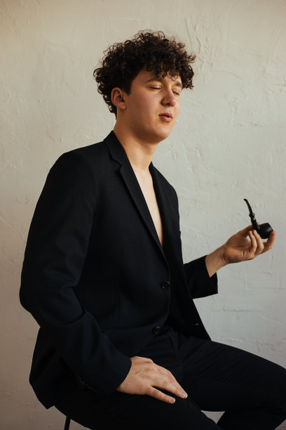 垂直复古肖像卷曲的黑发年轻人吸烟斗向下看，坐在演播室。复古的风格图片下载