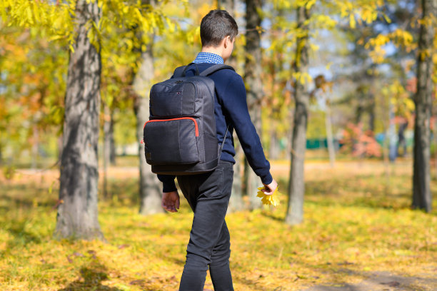 一个十几岁的男孩走过一个秋天的公园，在一个阳光明媚的日子里，树木的叶子都变黄了图片下载