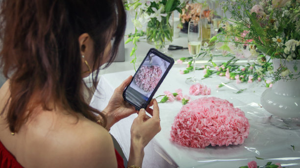 在花艺课上，一位美丽的亚洲女性正在完成自己的创作，并通过手机上的照片与老师的作品进行比较。图片下载
