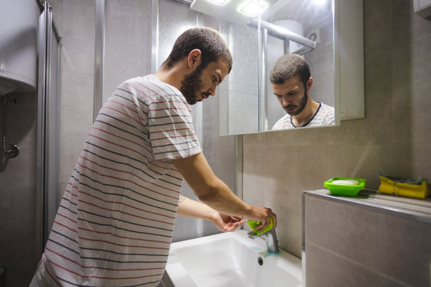 年轻开朗的男子正在用清洁布/抹布和清洁产品清洁浴室的水槽图片下载