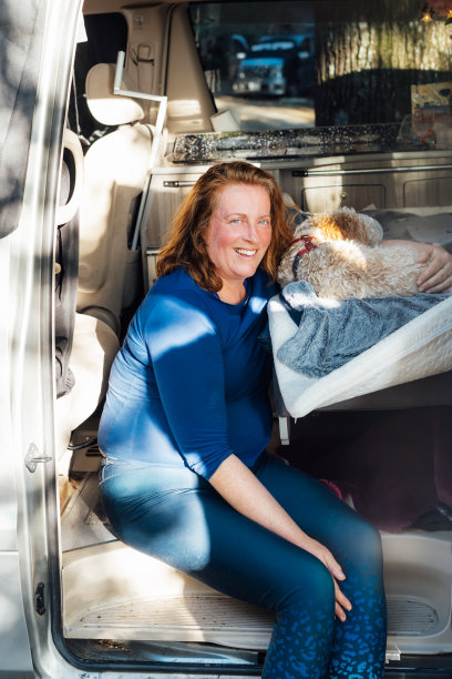 中年妇女在公路旅行中坐在厢式露营车里抱着她的小狗狗的照片。最好的朋友。享受自由的生活方式，假期，自由。带宠物旅行。图片下载