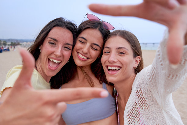 快乐的女性朋友们一起在海滩上，微笑着看着镜头，用手指比划着画面图片下载