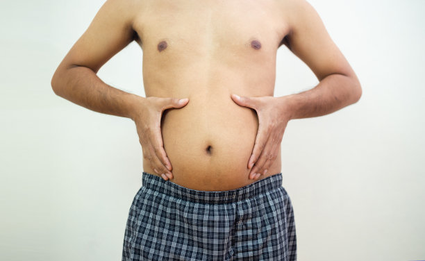 男人的手握着胖胖的肚子。身体超重。摄入过多的高热量食物。不健康的腰围与脂肪。缺乏锻炼。图片下载