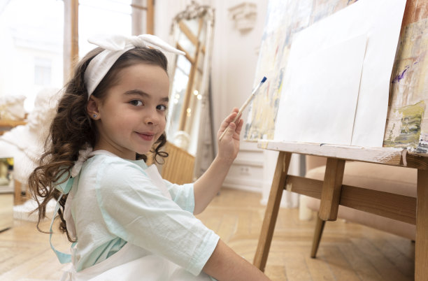 才华横溢的小艺术家看着镜头微笑，准备用画笔在画布上画画。艺术幼儿园。图片下载